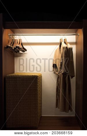 Brown bathrobe and wooden hanger in low light wooden wardrobe.