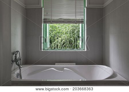 White bathtub in grey bathroom. Nature view from bathroom.