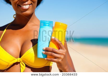 Žena v žluté bikiny nabízející suncream na pláži, aby se zabránilo spálení, důraz je na skladě, l