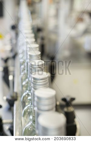A long row of glass bottles on the conveyor. The bottles are closed with a screw cap.