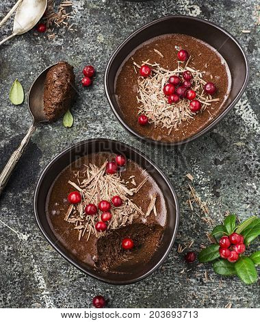 Homemade delicate chocolate mousse with cranberries and chocolate chips in serving ceramic bowls on a gray stone background. Top View
