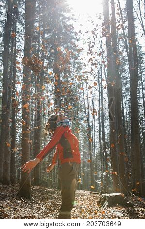 Athletic woman hiker enjoying the nature throwing leaves in autumn sunny forest. Nature lover active lifestyle happiness and fun concept.