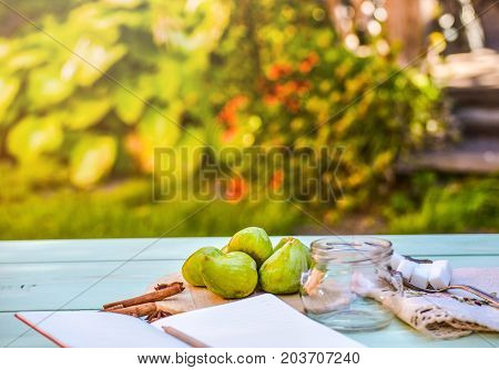 Still life with figs, jam cooking process. Fresh green figs on wooden backround, surrounded by spices, embroidered nupkin, vintage spoon, a glass container for jelly. Notebook with copy space.