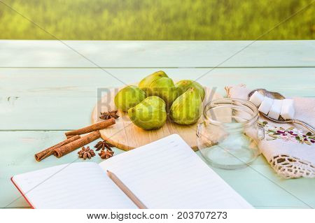 Still life with figs, jam cooking process. Fresh green figs on wooden backround, surrounded by spices, embroidered nupkin, vintage spoon, a glass container for jelly. Notebook with copy space.