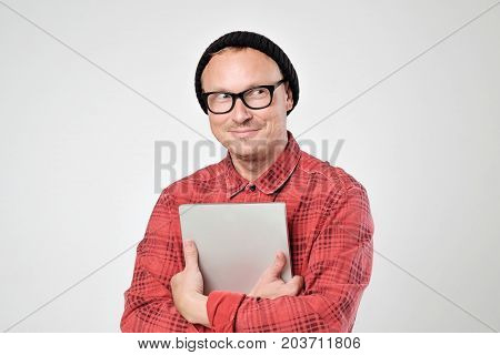A young programmer in a black hat is holding a laptop in his hands. He smiles and looks aside. Concept of positive human emotion