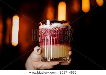 Close up glass of New York sour cocktail in a woman's hand at bar counter background.