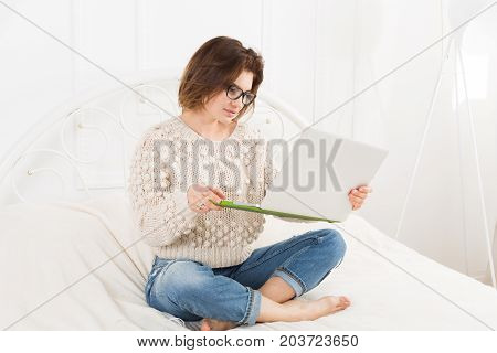 Young woman freelancer works at home in bed with laptop. Engrossed Girl in eyeglasses. Freelance.