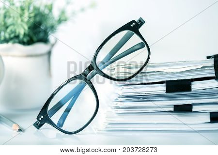 Close up black reading eyeglasses on stacking of office paper business working document and information data concept.