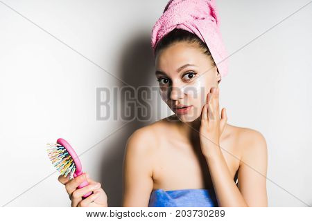 Young beautiful girl with a towel on her head looks surprised at the camera after a bath, holds in her hand a pink comb