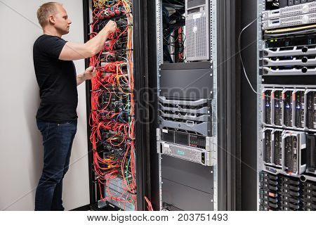 Side view of mid adult male IT technician checking with network cables connected to servers in datacenter