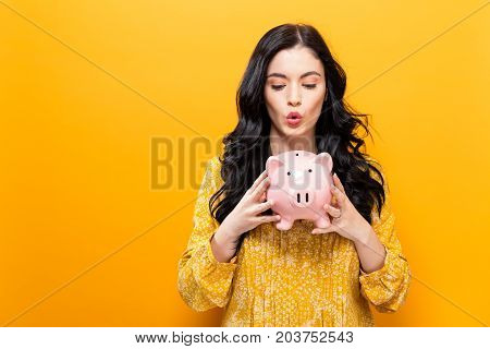 Young woman with a piggy bank on a yellow background