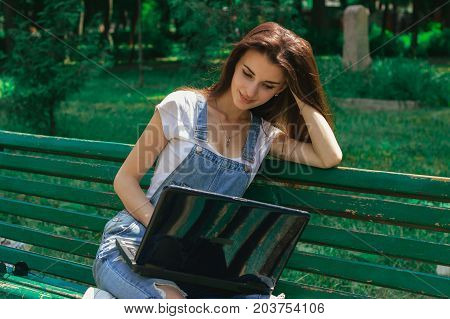 young sweet tired girl sits in the Park on a summer day and looks into the laptop