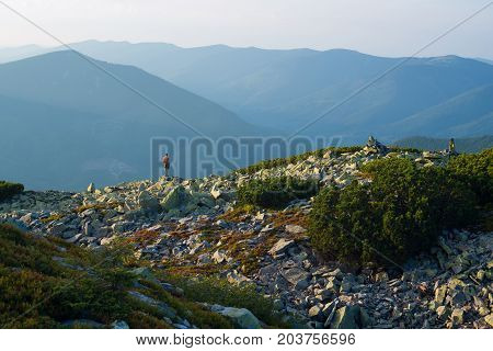 Lonely teenage boy stands on the edge of a rocky mountain range admiring the stunning panorama of the mountains in front of him at sunset. Epic travel in the mountains.