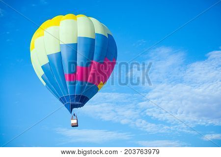 The big colorful hot air balloon is flying in the air on the cloudy sky.