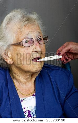 Senior lady having a temperature check with a digital thermometer by a health care worker.
