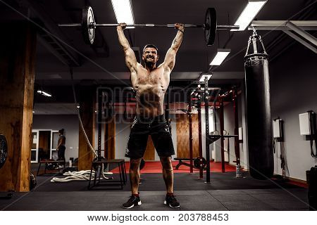 Muscular fitness man doing deadlift a barbell over his head in modern fitness center. Functional training. Snatch exercise