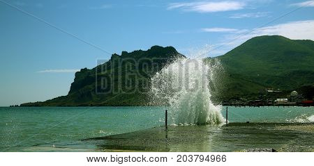The wave beats against the pier near the Kara-Dag mountain in the Crimea