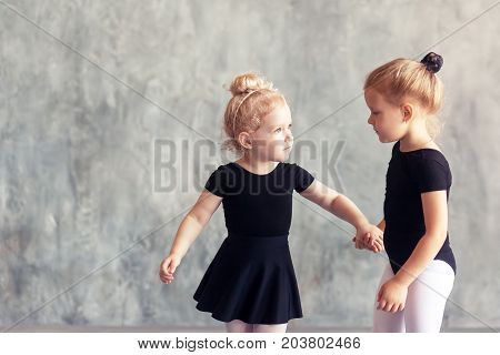 Two small fair-haired girls ballerinas in black packs white pantyhose white pointe shoes learn to dance a Russian ballet in a black dance studio
