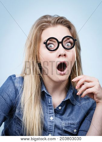 Happy shocked woman holding fake eyeglasses on stick having fun. Photo and carnival funny accessories concept.