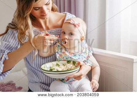 Closeup portrait of young woman mother feeding her girl daughter with vegetables broccoli cauliflower. Healthy organic food for children. Candid lifestyle family life. Baby trying finger food