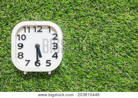 Closeup white clock for decorate show a half past five o'clock or 5:30 p.m. on green artificial grass floor textured background with copy space
