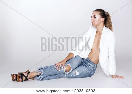 beautiful sexy tanned brunette woman with perfect makeup in white jacket and jeans posing in front of camera