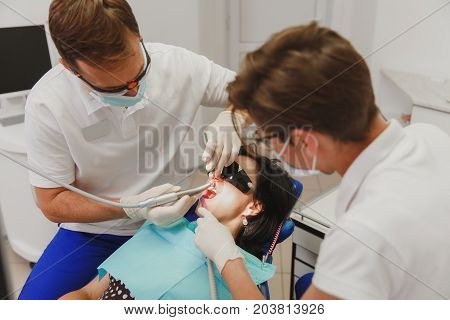 A Male Dentist With A Female Assistant Helps To Treat The Teeth Of A Woman Patient In A Clinic In Th