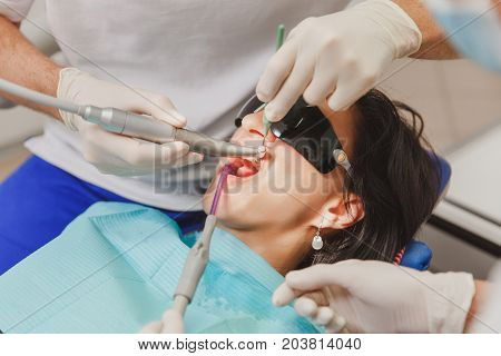The male dentist with a female assistant helps to treat the teeth of a woman patient in a clinic in the office close-up