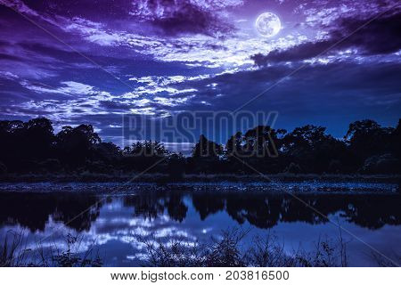 Sky With Many Star And Full Moon Above Silhouettes Of Trees And Lake.