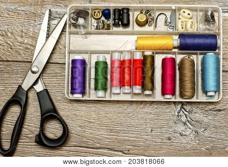 Sewing background: tailoring scissors,sewing toolbox and multicolor sewing threads on wooden table. Top view. Wooden texture.Template for designers