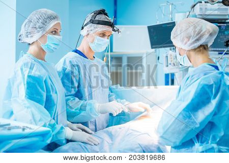 Believe me. Concentrated assistant standing in semi position and covering her face while putting hands on patient