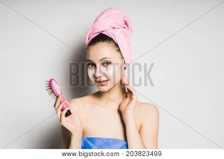Young girl after bathing with a towel on her head, holding a pink comb in her hand, smiling thoughtfully, looking at the camera