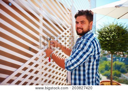 Young Adult Man Decorating The House Wall, By Setting Up The Wooden Trellis For Climbing Plants