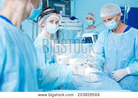 Strong anesthesia. Serious mature surgeon bowing head and standing near operating table while taking prick