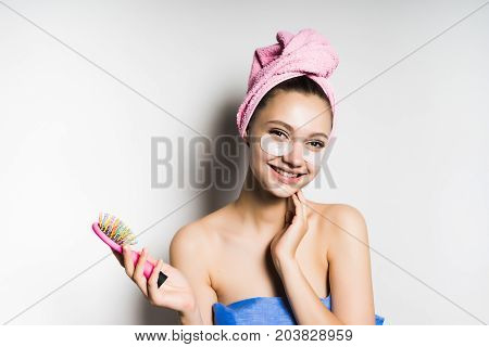 Young beautiful girl laughs, holds a comb in her hands, after a bath, with a towel on her head