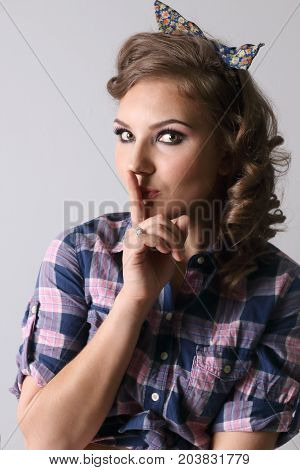 Pinup beautiful woman in checkered shirt shows hist gesture in studio