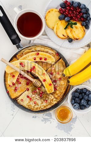 Sweet crepes with banana, honey and pomegranate seeds in a frying pan. Delicious family breakfast concept. Space for text