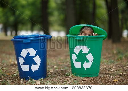 Blue and green bins. Cute preschooler boy, looking inside the trash bin in the street, summer outdoor, save the planet, save the Earth concept. Day in park. Funny babies.