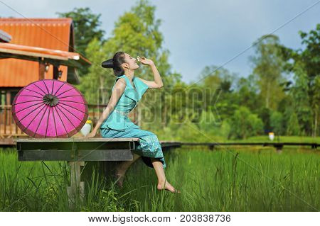 Young beautiful Lao woman in tradition dress sitting on wooden bridge in green rice field.