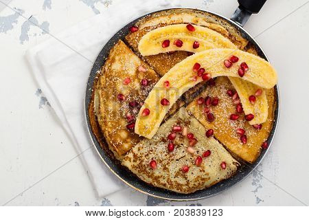 Sweet crepes with banana, honey and pomegranate seeds in a frying pan. Delicious family breakfast concept. Space for text