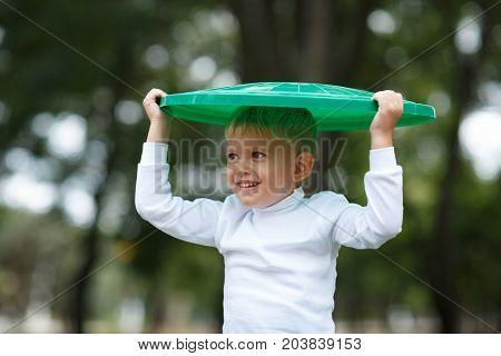Cute preschooler boy playing with the trash bin lid, in the street, summer outdoor, save the planet, save the Earth concept. Day in park. Funny babies.