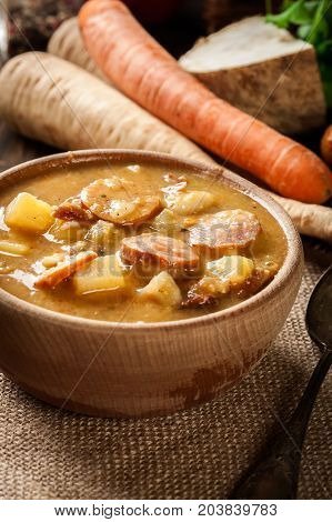 Wooden Bowl Of Split Pea Soup With Sausage And Potatoes