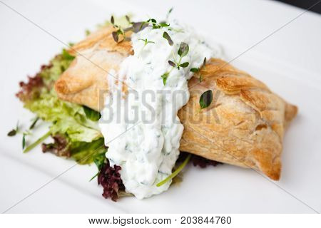 Traditional russian pie - coulibiac. Baked puff pastry filled with smoked salmon, served with sour cream sauce