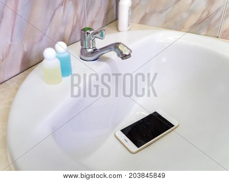 White smart phone droped in wash basin. Water damage waterproof concept.