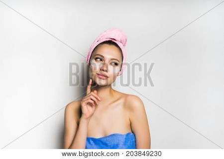 A young girl after bathing with a towel cunningly looks to the right, put her finger to her face. Isolated on white background