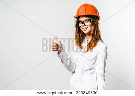 Young girl builder in an orange helmet is happy with something, raised her thumb