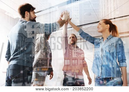 Unconquerable army. Group of young smart colleagues giving high five while standing in front of each other and expressing cheer