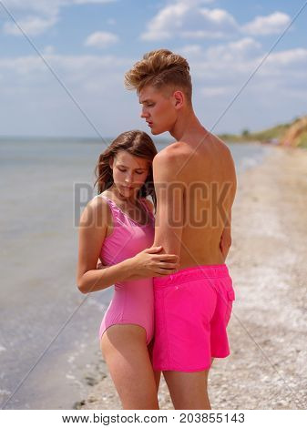 The woman is behind the man. Natural and sea view on the background. Joyful and romantic couple on sunset, at the golden beach, blue sky on the background. Sunny day outside. Love is in the air.