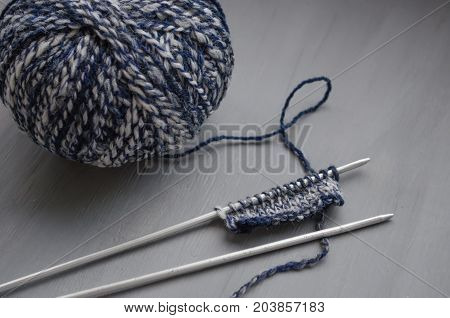 Woolen melange yarn and knitted pattern on knitting needles on a gray background