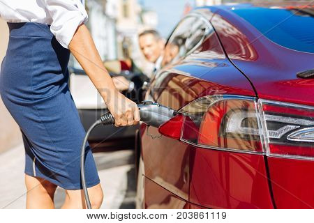 Refilling of the car. Selective focus of a fuel nozzle being held by a nice smart confident businesswoman while refilling the car